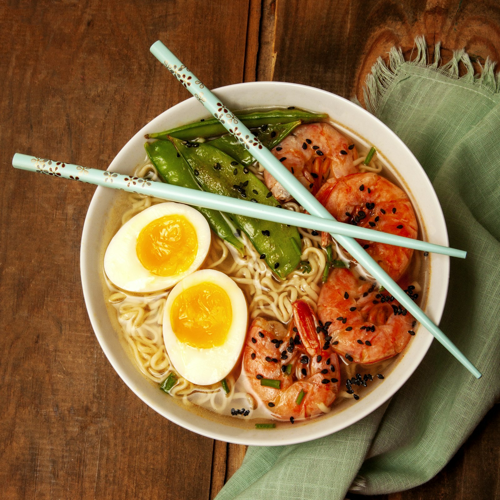 A bowl of Japanese ramen with egg, shrimp and snow peas
