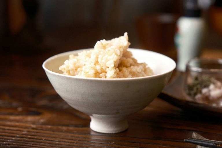 A white Japanese rice bowl (chawan) filled with rice on a wooden table