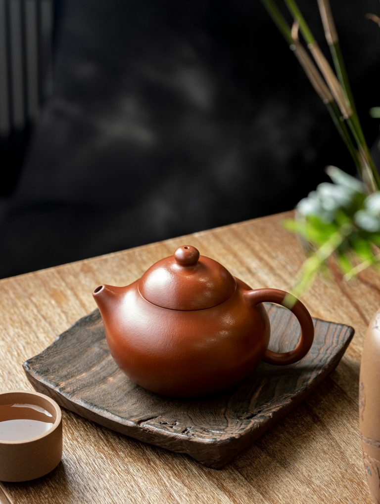 A red clay Japanese kyusu teapot on a wooden tray with a cup