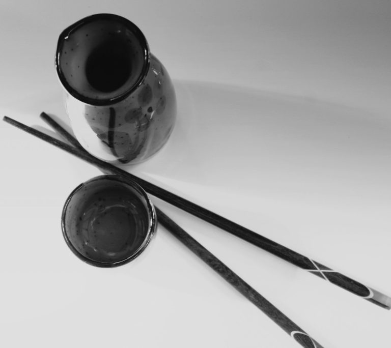 Sake being poured from a bottle into a small ceramic ochoko cup on a wooden table