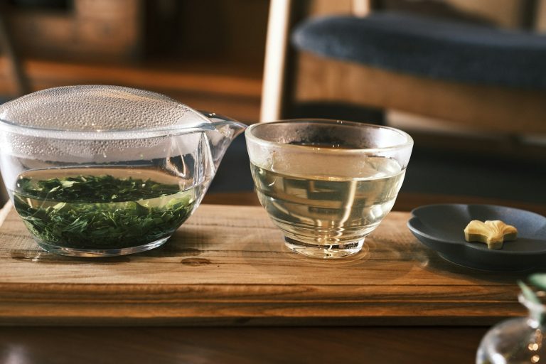 Japanese green tea in a glass pot with cups on a wooden tray