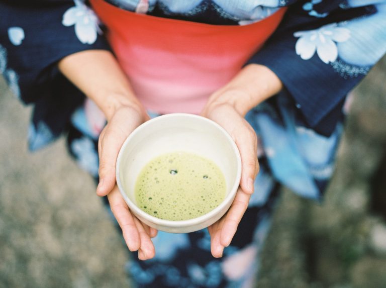 Two handleless Japanese yunomi teacups filled with green tea on a wooden surface