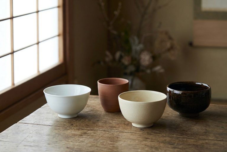 Four Japanese vessels with different clay bodies on a wooden table: glossy white porcelain, unglazed red stoneware, a pale crazed glaze and a thick dark glaze